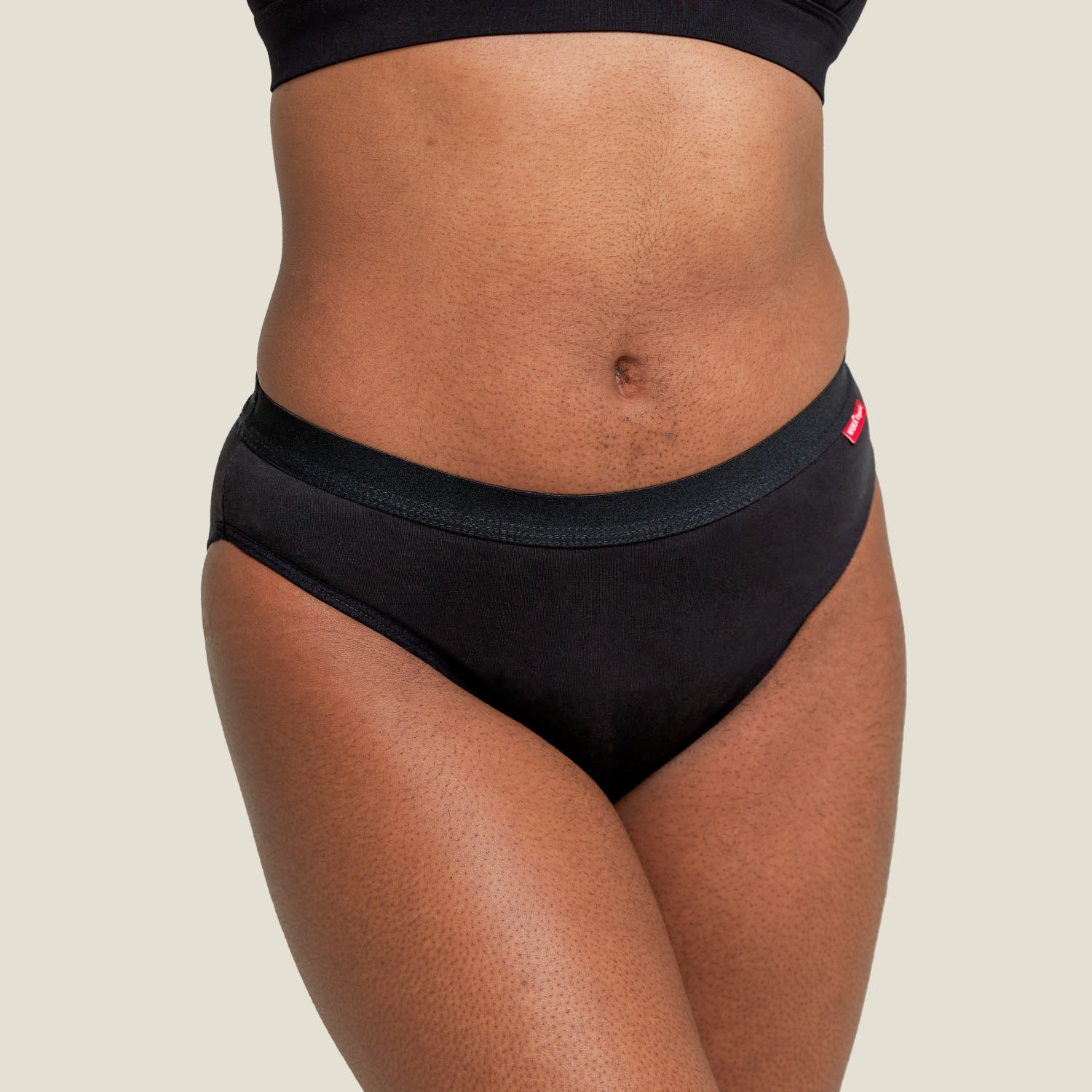 Close-up of WUKA Ultimate™ Bikini heavy flow period pants – smooth black organic cotton with signature red WUKA tag.