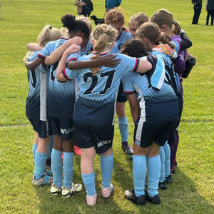 Girls’ football team huddle wearing WUKA period-proof sportswear, representing trusted club testimonials supporting girls to play confidently on their period